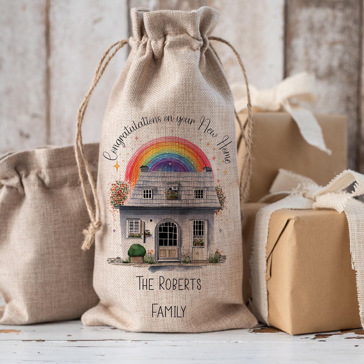 Drawstring Hessian Bottle Bag that reads Congratulations on your New Home with the family name at the bottom. The image in the middle is of a watercolour house with a rainbow behind it.